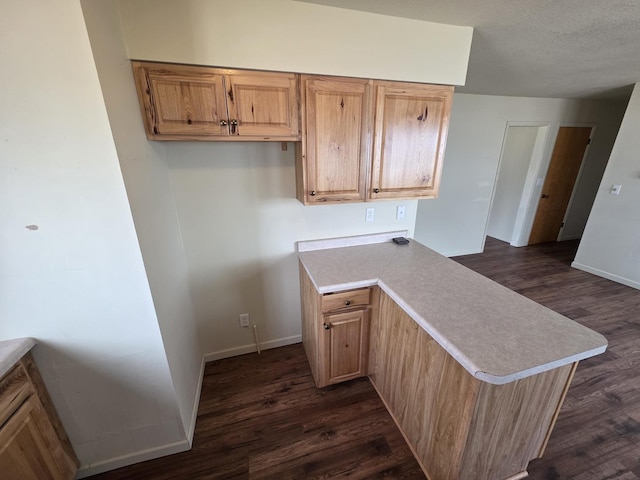 kitchen with a peninsula, light countertops, dark wood-type flooring, and baseboards