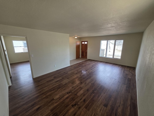 empty room with baseboards, a textured ceiling, and dark wood finished floors