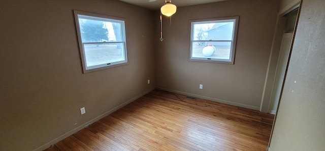 unfurnished bedroom featuring light wood-type flooring, multiple windows, baseboards, and visible vents