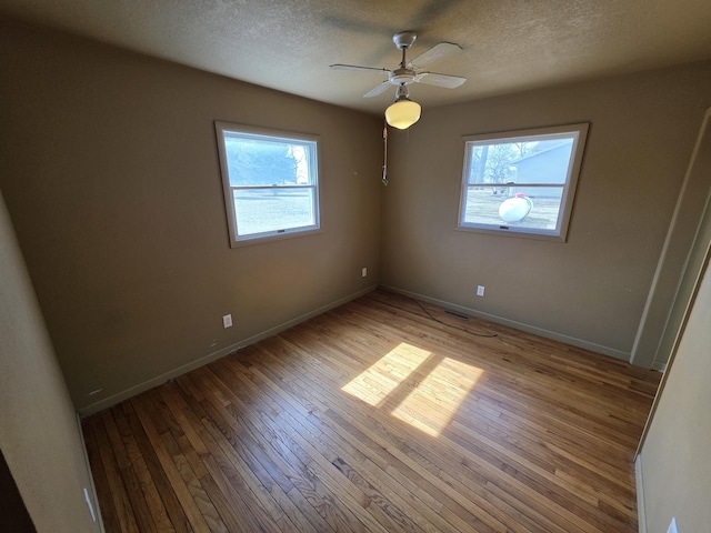 interior space featuring hardwood / wood-style floors, a ceiling fan, visible vents, baseboards, and a textured ceiling