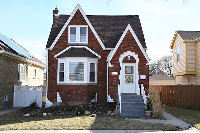 tudor-style house featuring fence, brick siding, a chimney, and entry steps