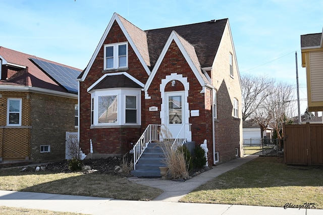 english style home featuring brick siding, a front yard, and fence