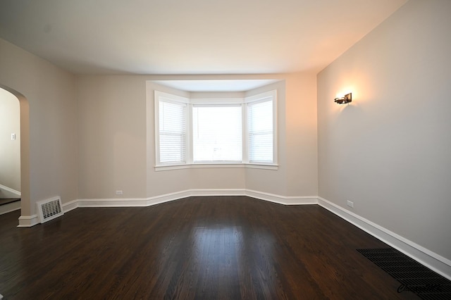 spare room featuring visible vents, arched walkways, baseboards, and dark wood-style floors