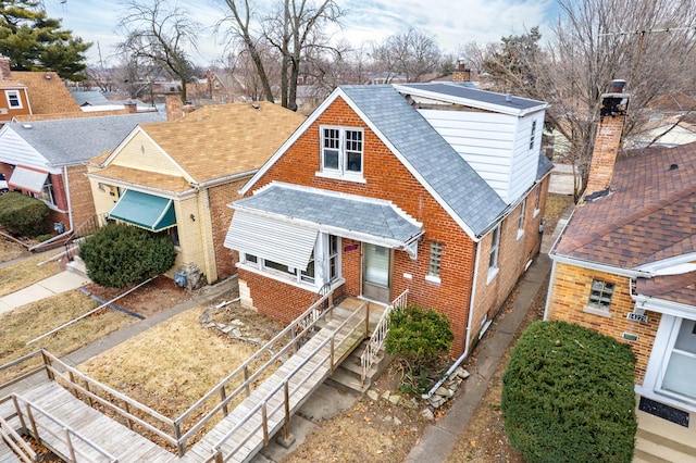 view of front facade featuring brick siding, roof with shingles, and a chimney