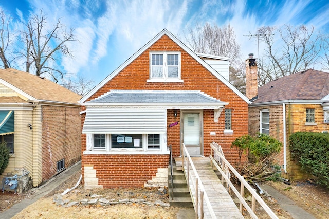 view of front of home with brick siding, roof with shingles, and a chimney