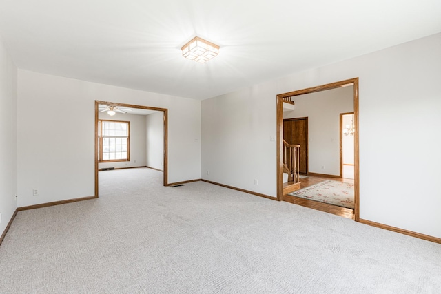 empty room featuring light carpet, stairs, and baseboards