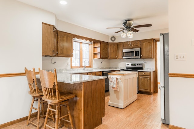 kitchen with ceiling fan, light wood-style flooring, appliances with stainless steel finishes, a peninsula, and a sink