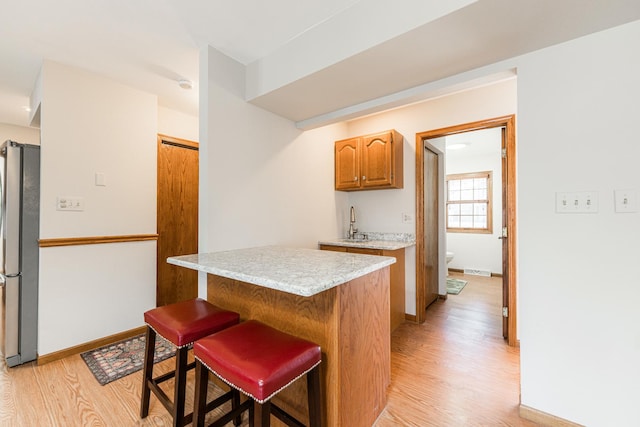 kitchen with light wood-type flooring, a breakfast bar area, light countertops, and freestanding refrigerator