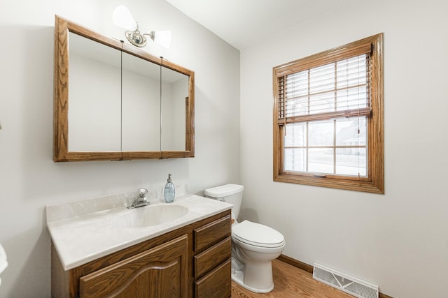 bathroom featuring visible vents, baseboards, toilet, wood finished floors, and vanity