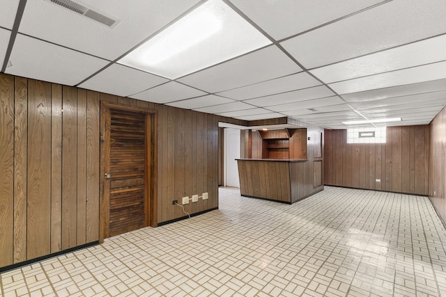 bar with visible vents, wood walls, baseboards, and a drop ceiling