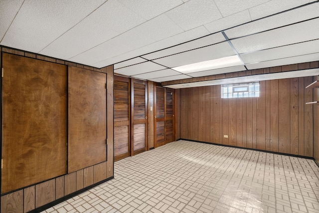 basement featuring wooden walls, baseboards, and a drop ceiling