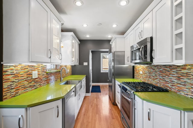 kitchen with a sink, backsplash, stainless steel appliances, white cabinets, and light wood finished floors