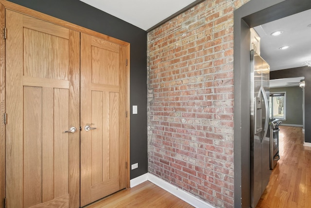 interior space with brick wall, baseboards, and light wood finished floors