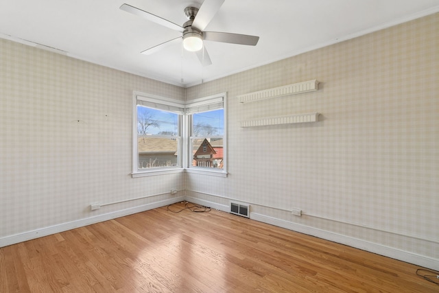 empty room with wood finished floors, visible vents, baseboards, wallpapered walls, and ceiling fan