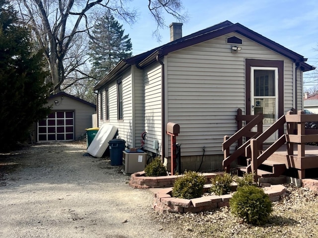 view of side of property with an outbuilding, a chimney, and driveway