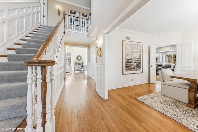 foyer entrance with light wood-type flooring, visible vents, and crown molding