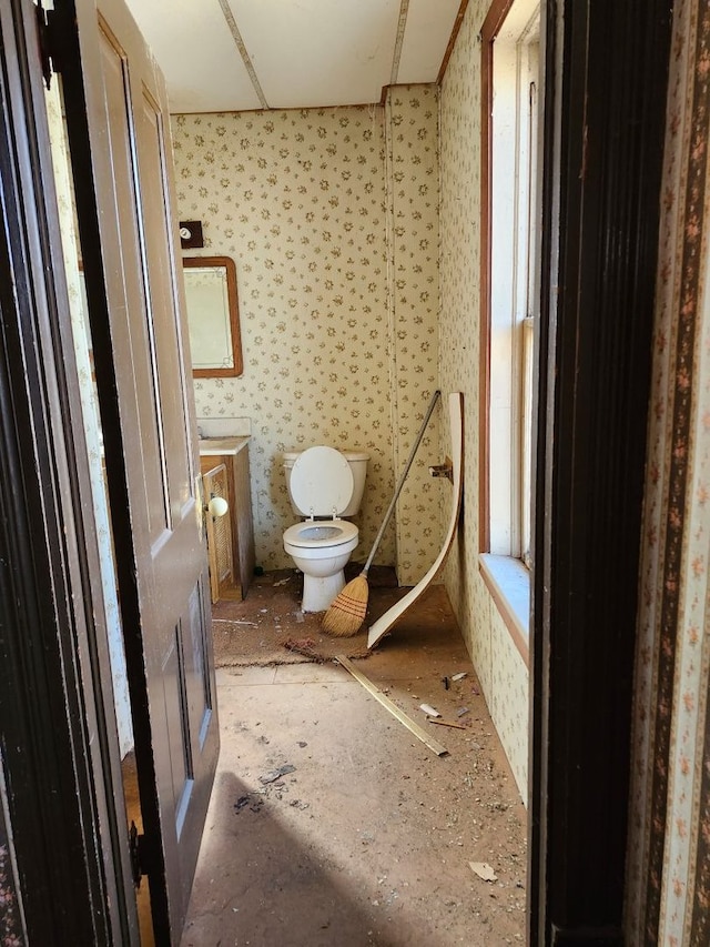 half bathroom featuring wallpapered walls, toilet, and vanity