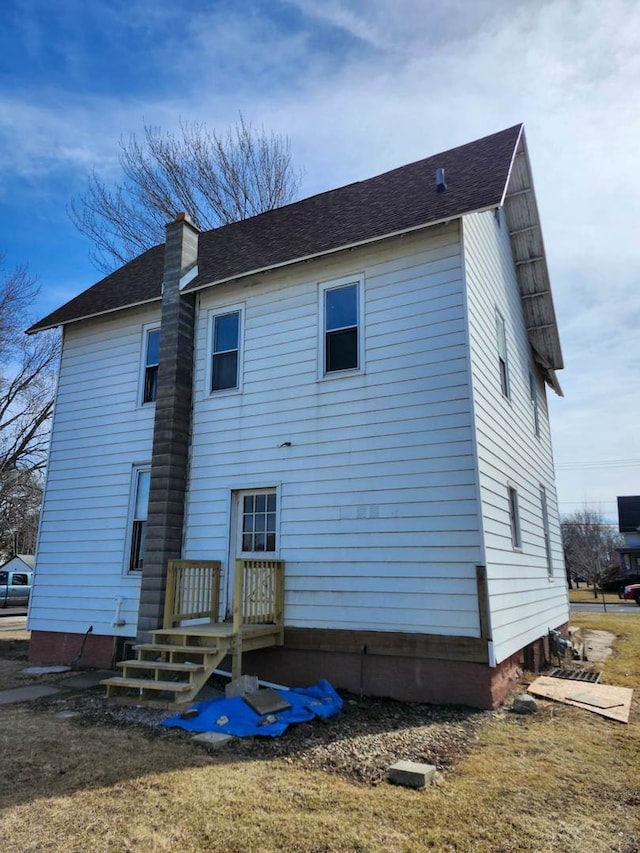 rear view of property featuring a chimney and roof with shingles