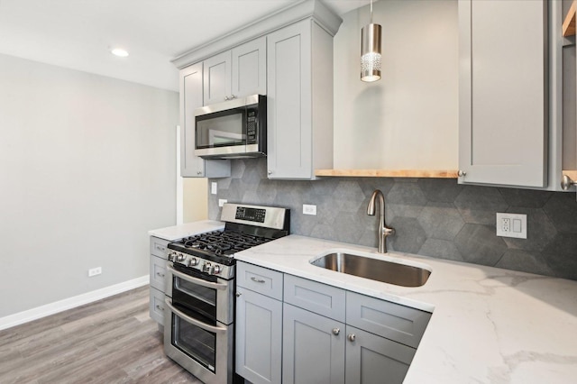 kitchen featuring light stone countertops, gray cabinets, a sink, appliances with stainless steel finishes, and backsplash