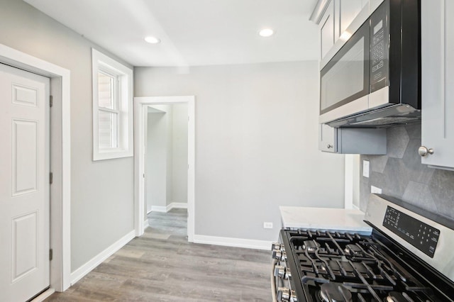 kitchen with stainless steel gas stove, light wood-style flooring, tasteful backsplash, and baseboards