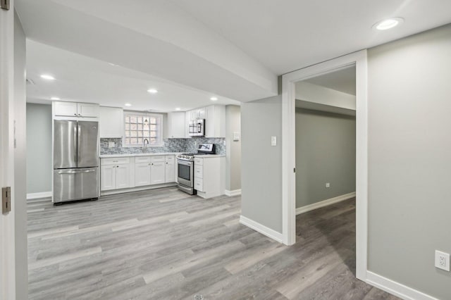 kitchen with light wood-type flooring, a sink, tasteful backsplash, white cabinetry, and stainless steel appliances