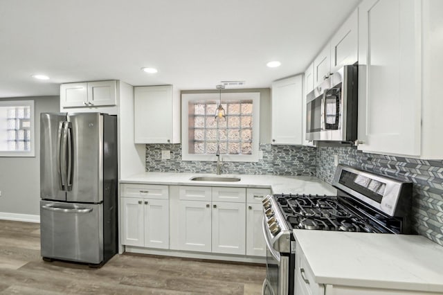 kitchen featuring a sink, decorative backsplash, stainless steel appliances, white cabinets, and light wood-type flooring