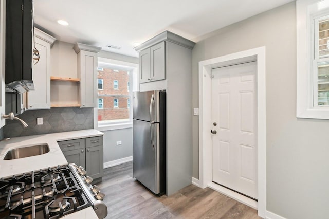 kitchen with decorative backsplash, gray cabinets, wood finished floors, stainless steel appliances, and a sink