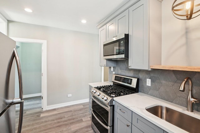 kitchen featuring a sink, decorative backsplash, gray cabinetry, stainless steel appliances, and light wood-type flooring