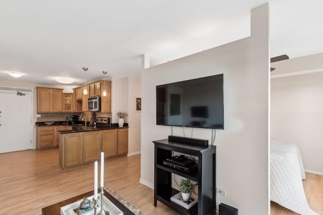 kitchen with dark countertops, a sink, glass insert cabinets, stainless steel microwave, and light wood-type flooring