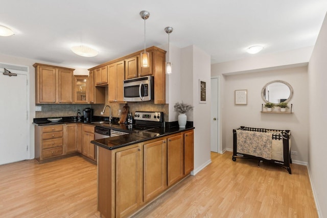 kitchen featuring light wood finished floors, a peninsula, stainless steel appliances, tasteful backsplash, and brown cabinets