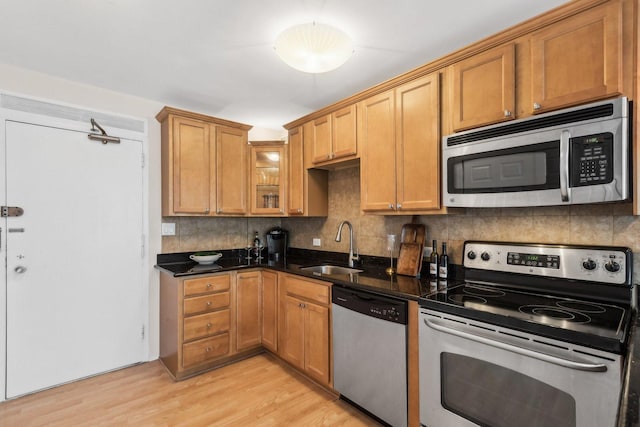 kitchen with light wood-style flooring, a sink, backsplash, stainless steel appliances, and glass insert cabinets