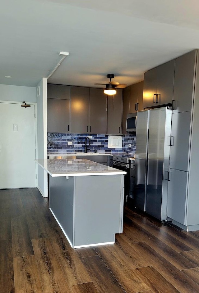 kitchen featuring stainless steel appliances, backsplash, dark wood-style flooring, and light countertops