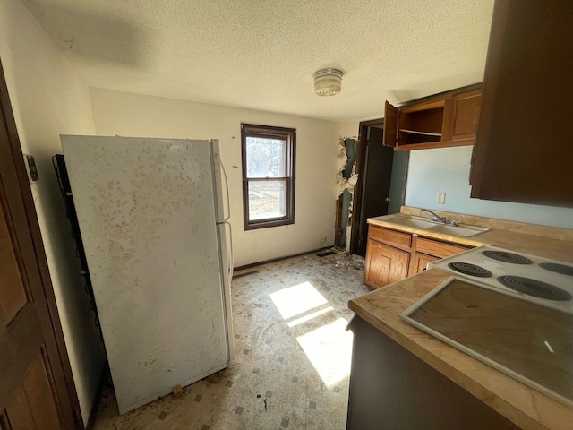 kitchen featuring a sink, freestanding refrigerator, brown cabinetry, a textured ceiling, and open shelves