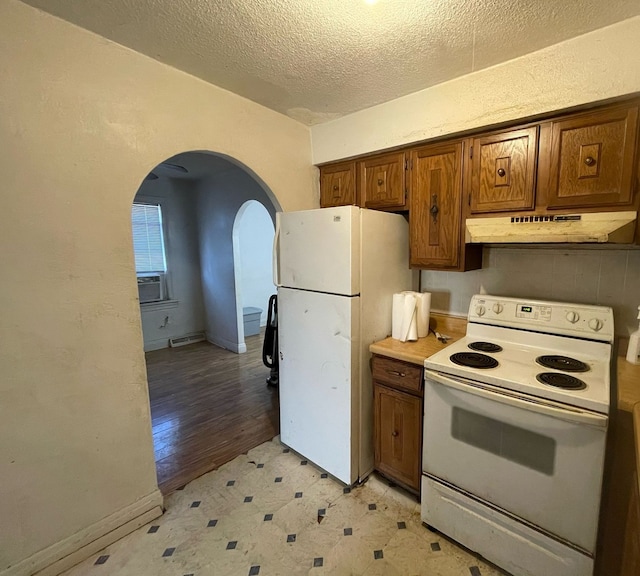 kitchen with under cabinet range hood, brown cabinets, white appliances, and arched walkways