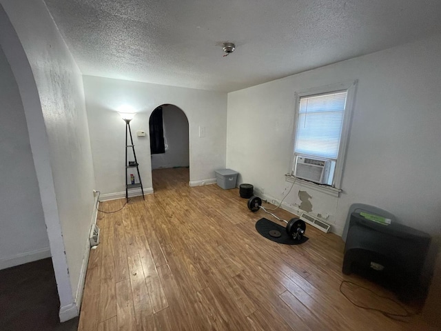 empty room featuring hardwood / wood-style flooring, a textured ceiling, cooling unit, arched walkways, and baseboards