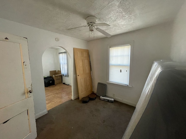 interior space featuring a ceiling fan, baseboards, carpet floors, arched walkways, and a textured ceiling