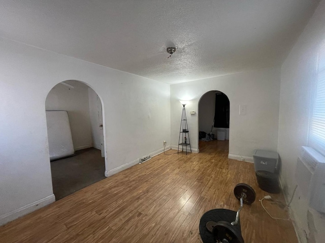 unfurnished room featuring baseboards, arched walkways, a textured ceiling, and wood finished floors