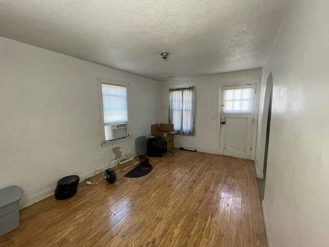 unfurnished living room featuring cooling unit, baseboards, arched walkways, hardwood / wood-style flooring, and a textured ceiling