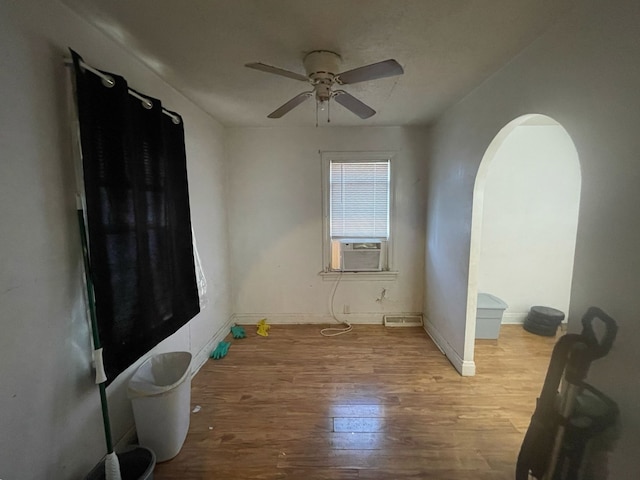 bedroom with cooling unit, wood finished floors, baseboards, arched walkways, and ceiling fan