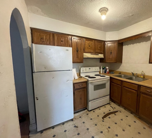 kitchen with under cabinet range hood, a sink, white appliances, arched walkways, and light floors