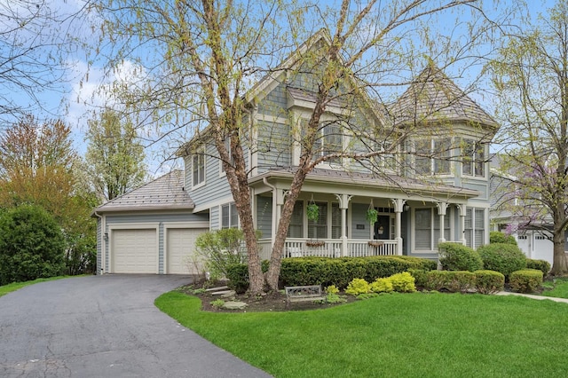 victorian house featuring driveway, a porch, a front lawn, and an attached garage