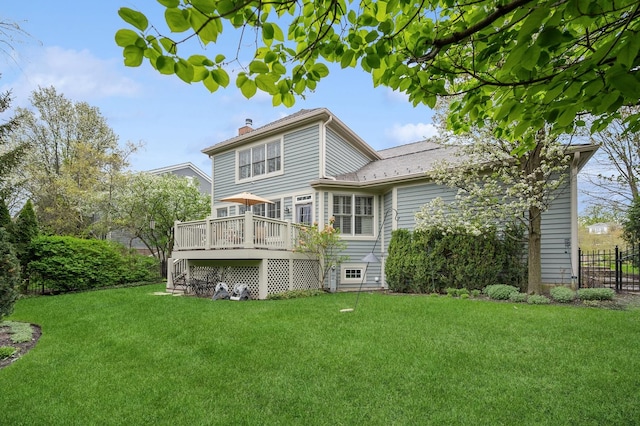 back of property with a wooden deck, a chimney, fence, and a lawn