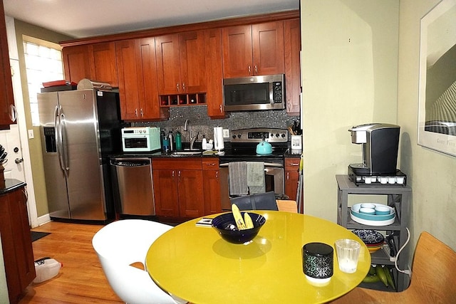 kitchen featuring a sink, light wood-style floors, appliances with stainless steel finishes, dark countertops, and tasteful backsplash