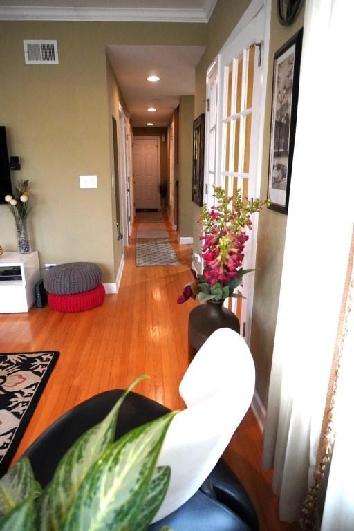 hallway featuring crown molding, wood finished floors, visible vents, and baseboards