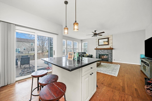kitchen featuring visible vents, a ceiling fan, dark countertops, wood finished floors, and a stone fireplace
