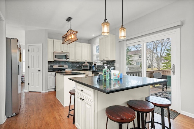 kitchen with a breakfast bar, light wood-style flooring, a kitchen island, stainless steel appliances, and decorative backsplash