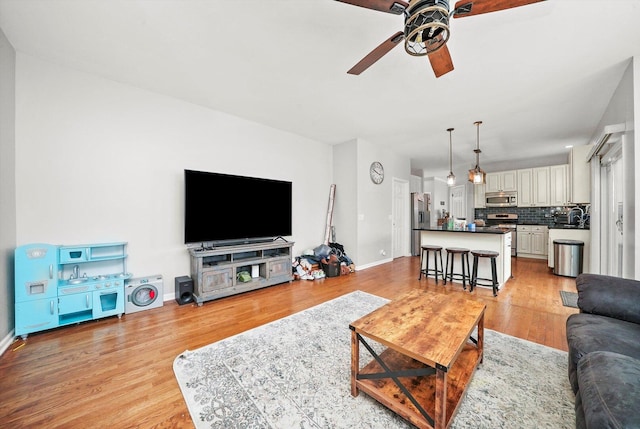 living room featuring light wood finished floors, baseboards, and ceiling fan