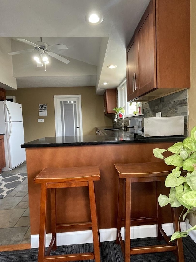 kitchen with backsplash, a kitchen bar, a peninsula, freestanding refrigerator, and a sink