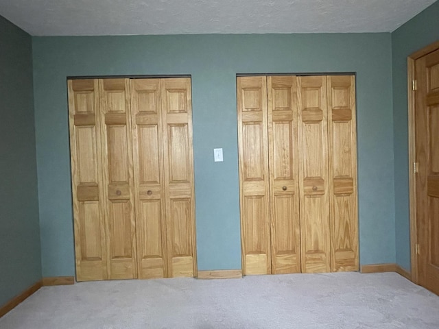 bedroom with baseboards, carpet floors, two closets, and a textured ceiling