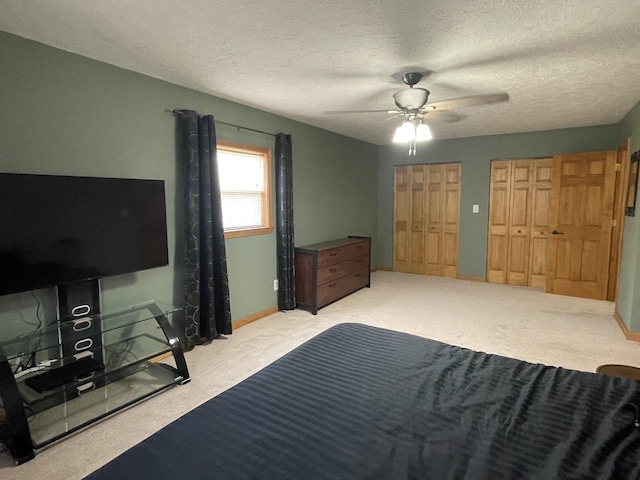 bedroom featuring ceiling fan, carpet flooring, two closets, and a textured ceiling